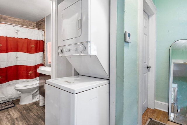 full bath with toilet, curtained shower, stacked washer / dryer, and wood finished floors