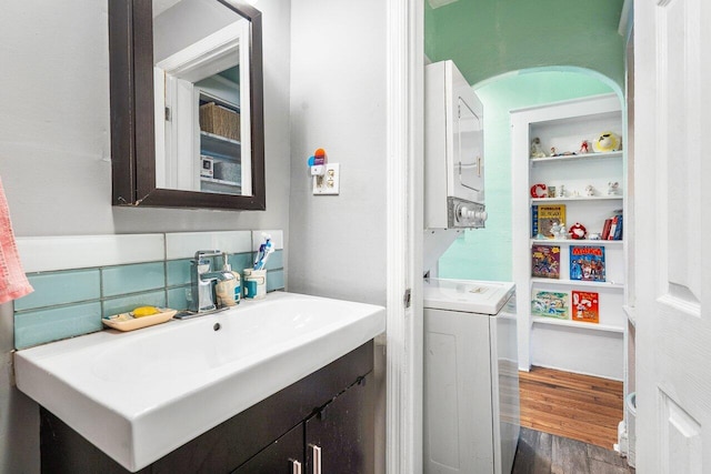 bathroom with vanity, stacked washer / dryer, wood finished floors, and backsplash