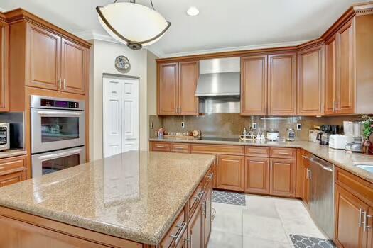 kitchen with wall chimney exhaust hood, a kitchen island, appliances with stainless steel finishes, light stone countertops, and backsplash