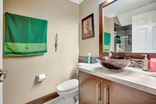 bathroom with tasteful backsplash, a shower with shower door, vanity, and toilet