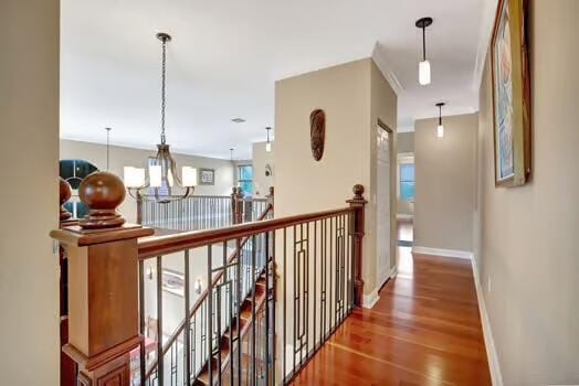 corridor with a chandelier, wood finished floors, an upstairs landing, and baseboards