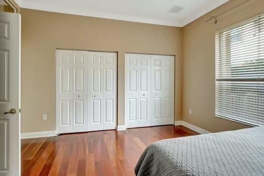 bedroom with baseboards, wood finished floors, and multiple closets