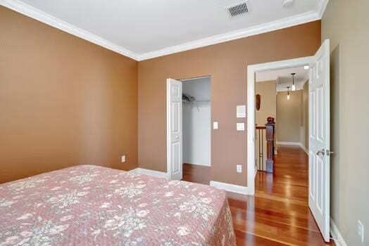 bedroom with baseboards, wood finished floors, visible vents, and crown molding