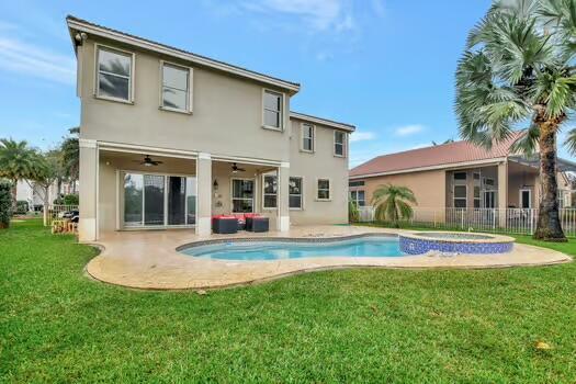 back of property with a lawn, fence, a ceiling fan, and stucco siding