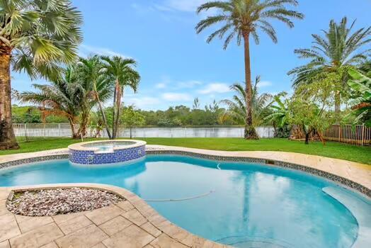 view of pool featuring a lawn, a water view, a fenced backyard, and a pool with connected hot tub