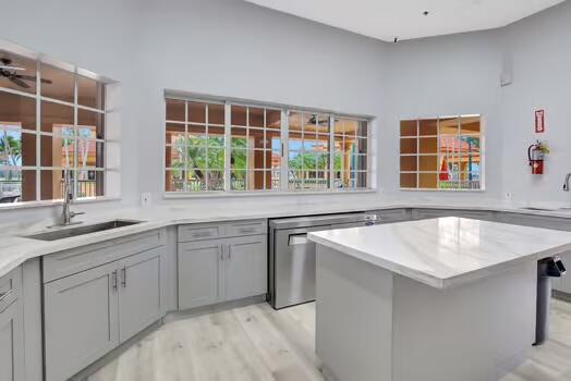 kitchen featuring dishwasher, a center island, gray cabinets, light wood-type flooring, and a sink