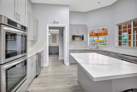 kitchen featuring light wood finished floors, gray cabinets, appliances with stainless steel finishes, a sink, and a kitchen island