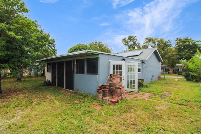 rear view of house with roof mounted solar panels, a lawn, and stucco siding