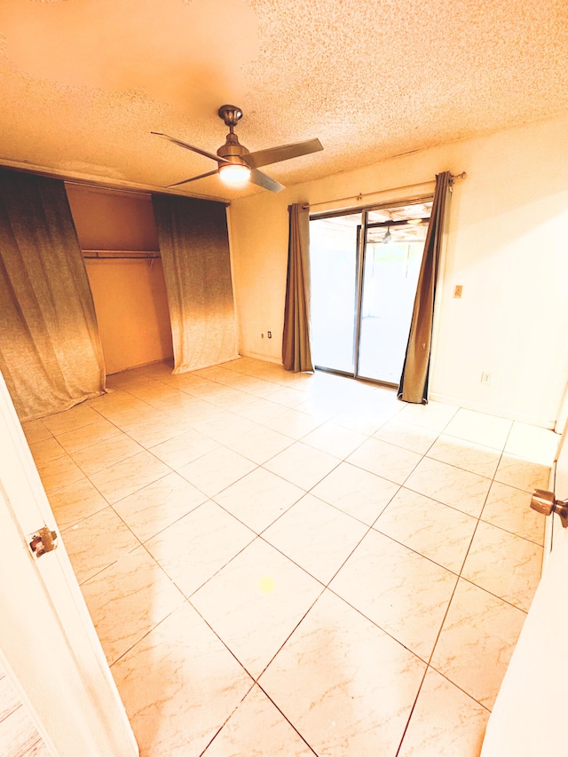 empty room featuring a ceiling fan, a textured ceiling, and light tile patterned flooring