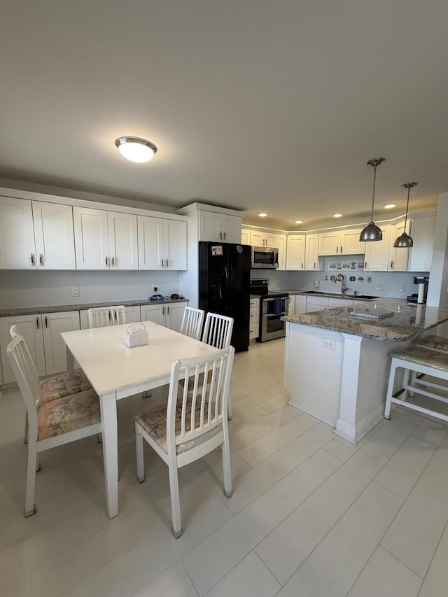 kitchen with a peninsula, dark stone counters, appliances with stainless steel finishes, white cabinetry, and decorative light fixtures