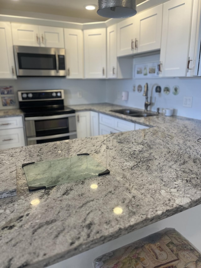 kitchen with appliances with stainless steel finishes, a sink, light stone counters, and white cabinets