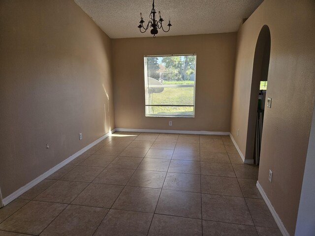 tiled spare room featuring baseboards, arched walkways, a textured ceiling, and an inviting chandelier