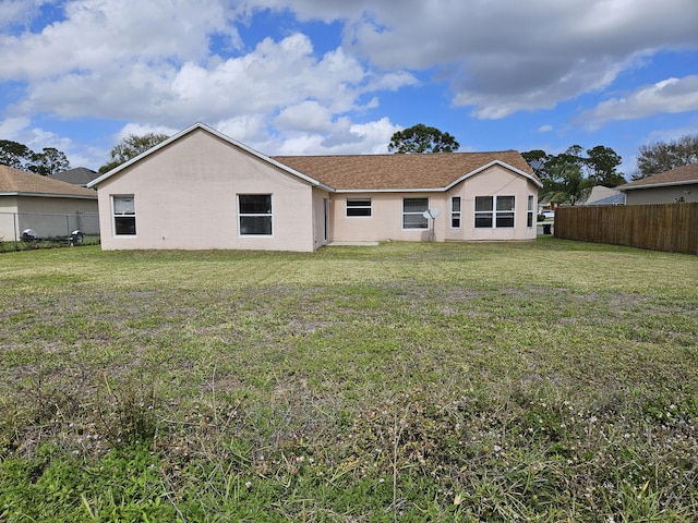 rear view of property with stucco siding, a lawn, and fence