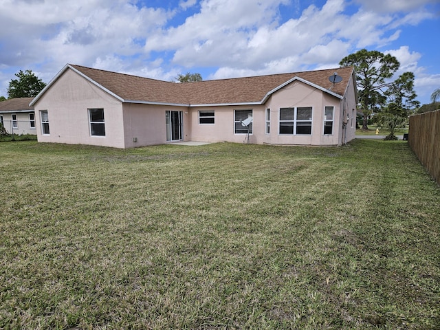 rear view of property featuring stucco siding, a yard, and fence