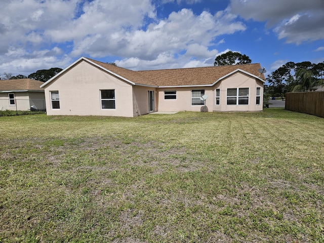 rear view of house featuring stucco siding, a yard, and fence