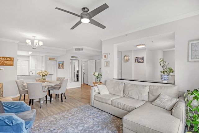 living area featuring crown molding, light wood finished floors, visible vents, baseboards, and ceiling fan with notable chandelier