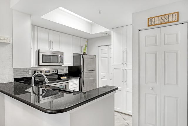 kitchen with stainless steel appliances, a peninsula, white cabinets, backsplash, and dark stone counters