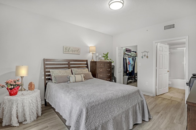 bedroom featuring visible vents, baseboards, a closet, light wood finished floors, and a walk in closet