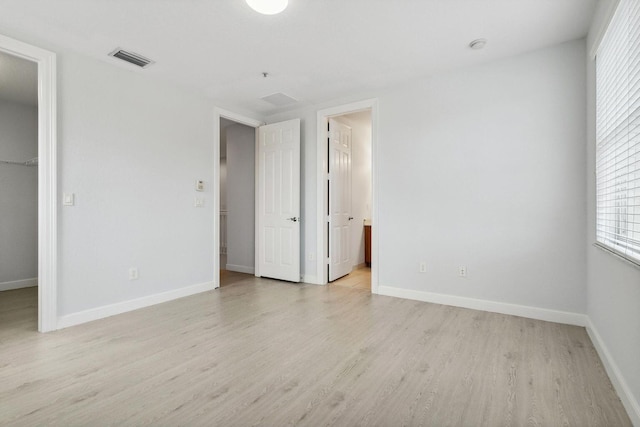 unfurnished bedroom with light wood-style flooring, visible vents, a walk in closet, and baseboards