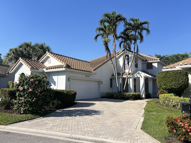 mediterranean / spanish house featuring a garage, decorative driveway, a tile roof, and stucco siding