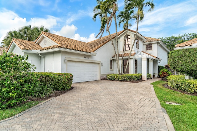 mediterranean / spanish home with a tiled roof, decorative driveway, an attached garage, and stucco siding