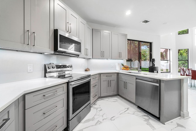 kitchen featuring gray cabinetry, a peninsula, visible vents, marble finish floor, and appliances with stainless steel finishes