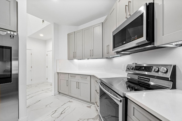 kitchen with gray cabinetry, baseboards, marble finish floor, appliances with stainless steel finishes, and light countertops