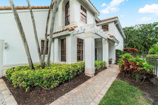 view of property exterior featuring a tile roof, fence, and stucco siding