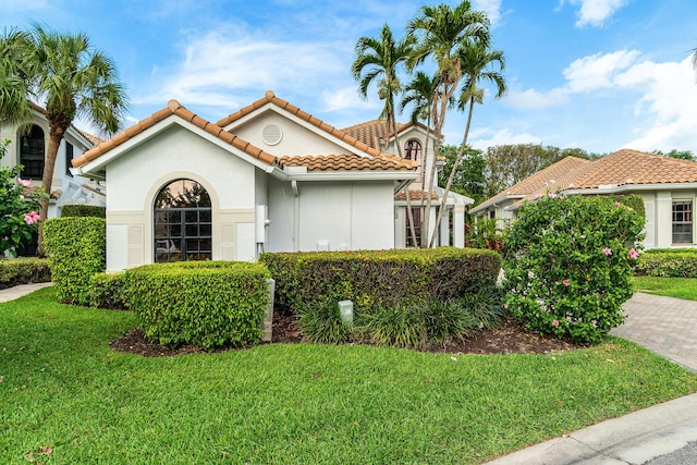 mediterranean / spanish-style house with decorative driveway, a tiled roof, a front lawn, and stucco siding