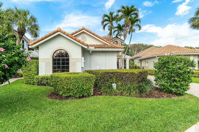 mediterranean / spanish house featuring a tile roof, driveway, a front lawn, and stucco siding