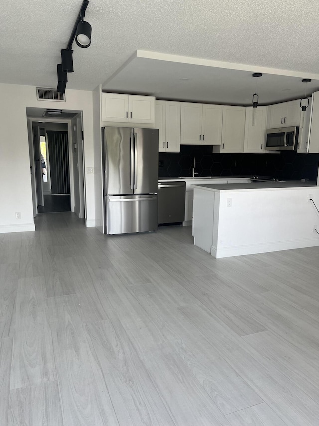 kitchen featuring a textured ceiling, white cabinetry, light wood-style floors, appliances with stainless steel finishes, and backsplash