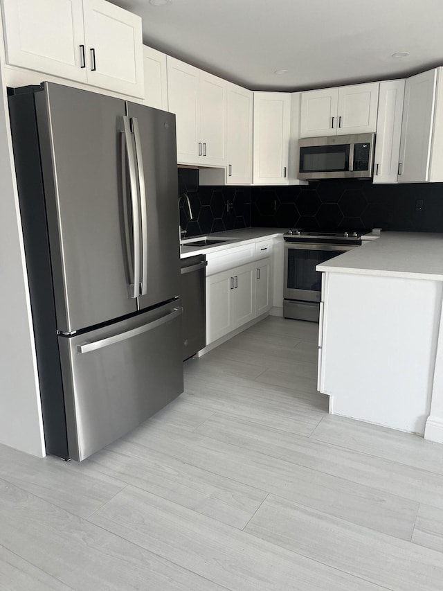 kitchen featuring stainless steel appliances, a sink, white cabinets, and decorative backsplash