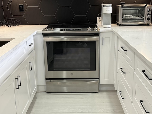 details with electric range, backsplash, white cabinetry, and a toaster