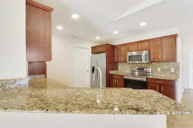 kitchen featuring a peninsula, appliances with stainless steel finishes, backsplash, and light stone countertops