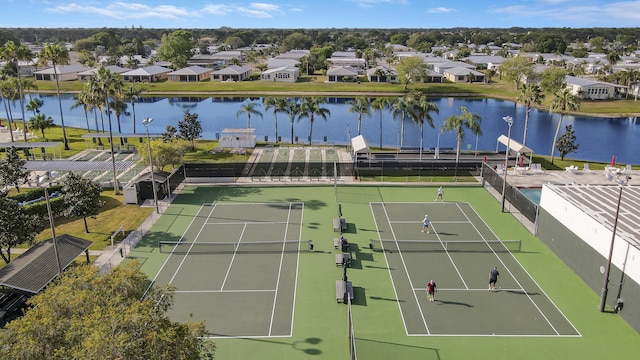 view of tennis court with a residential view, a water view, and fence