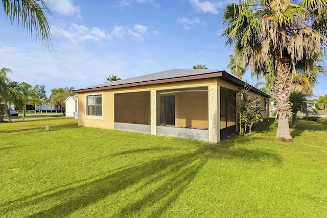 rear view of property with a yard, a sunroom, and stucco siding