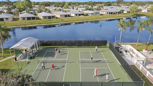 view of tennis court with a residential view, a water view, and fence