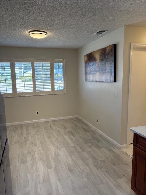 empty room featuring light wood-type flooring, baseboards, a textured ceiling, and visible vents