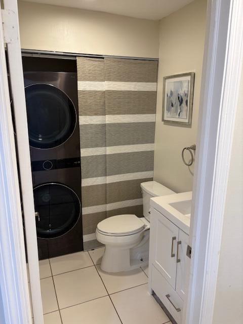 half bath featuring vanity, tile patterned floors, toilet, and stacked washer / drying machine