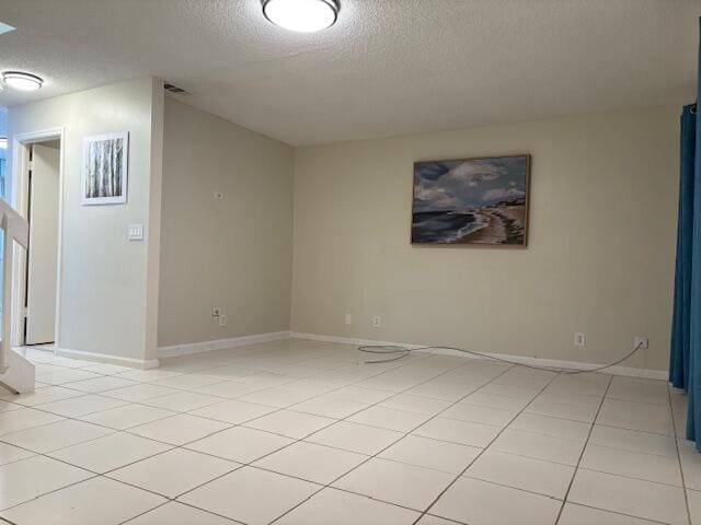 spare room with light tile patterned flooring, visible vents, a textured ceiling, and baseboards