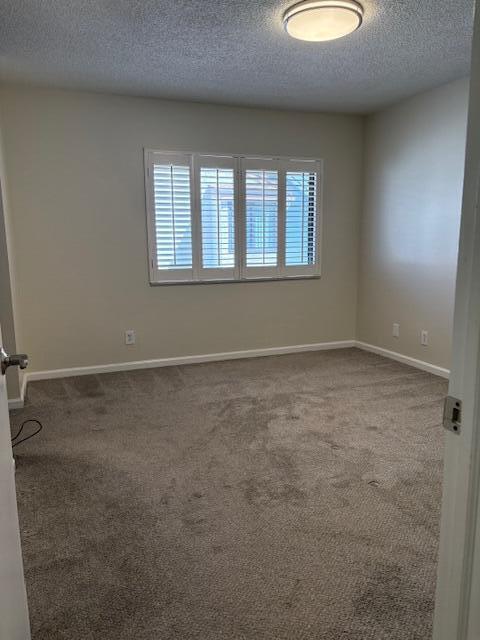 unfurnished room with a textured ceiling, baseboards, and dark colored carpet