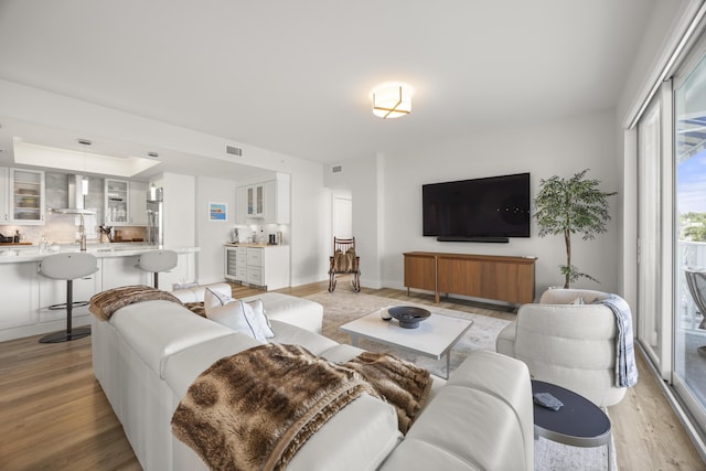 living room featuring light wood-style floors, baseboards, visible vents, and a raised ceiling