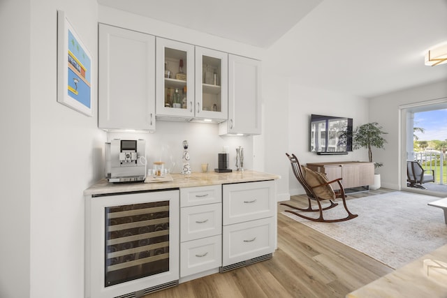 bar featuring beverage cooler, baseboards, light wood-style flooring, and a bar