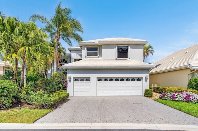 traditional-style house featuring a garage, stucco siding, decorative driveway, and a tiled roof