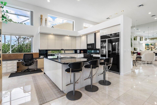 kitchen featuring dark countertops, a sink, a high ceiling, black appliances, and built in desk