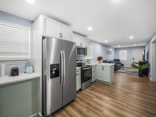 kitchen featuring white cabinets, open floor plan, dark wood-type flooring, a peninsula, and stainless steel appliances