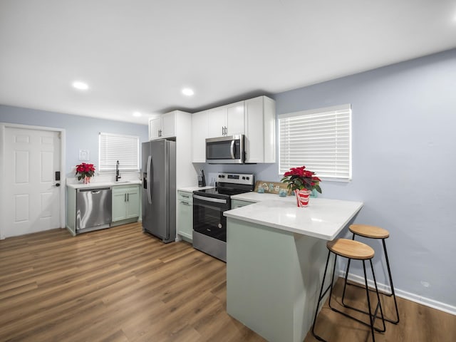 kitchen featuring dark wood-style floors, a breakfast bar, stainless steel appliances, light countertops, and a peninsula