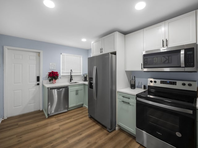 kitchen featuring stainless steel appliances, a sink, wood finished floors, white cabinetry, and light countertops