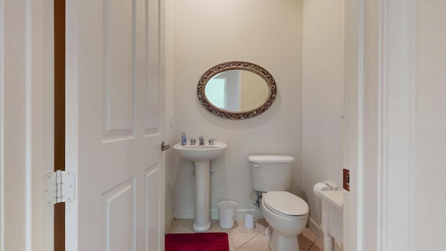 half bathroom featuring toilet, tile patterned flooring, baseboards, and a sink