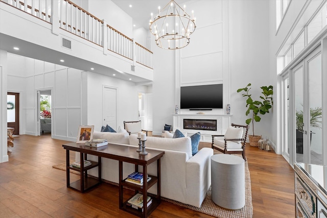 living area with a notable chandelier, dark wood-style flooring, a towering ceiling, visible vents, and a glass covered fireplace